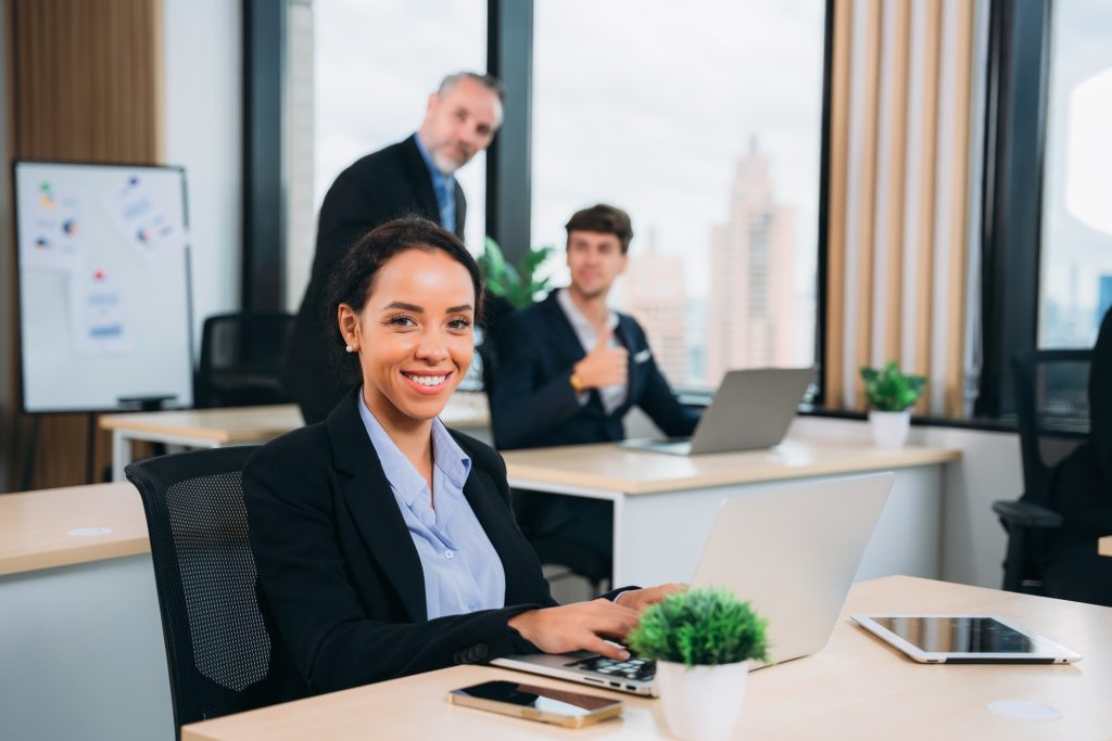 A group of different business people are sitting around a big meeting table in a modern office.