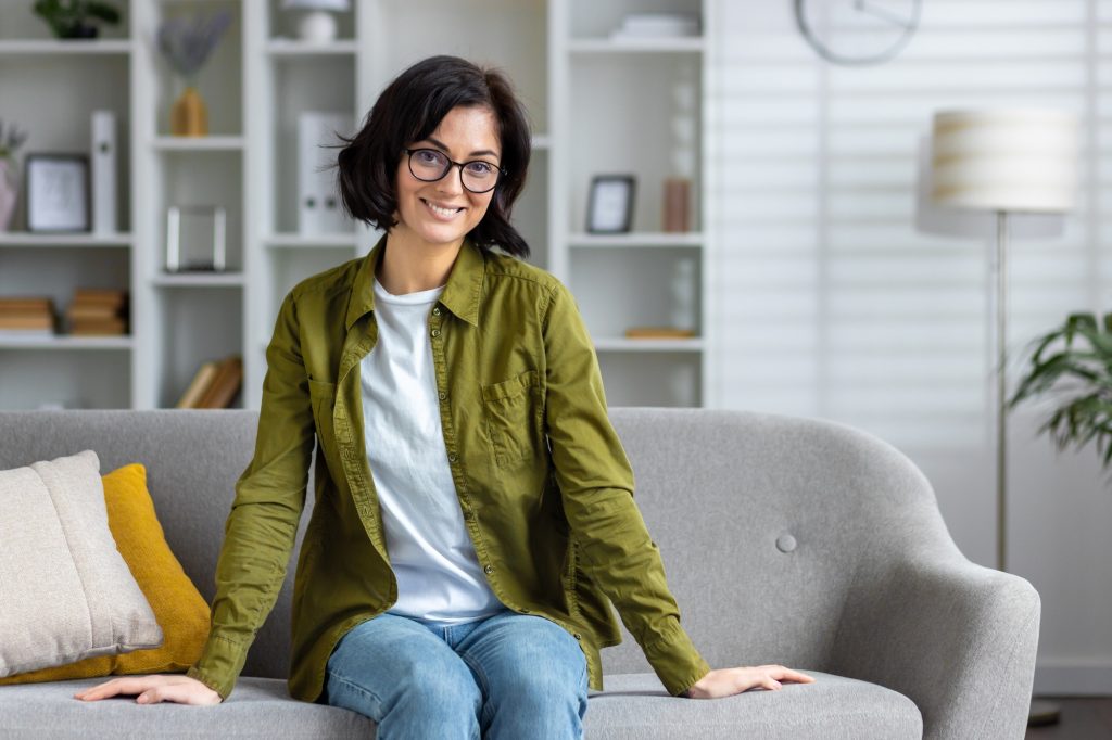 Confident modern woman smiling and sitting on sofa at stylish home interior